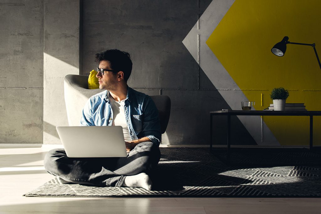 imagem de um jovem sentado no tapete com o notebook no colo