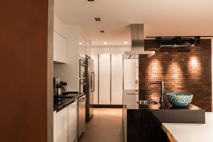 imagem de uma cozinha moderna com ilha e uma parede de tijolos a vista ao lado, com iluminação direcionadae