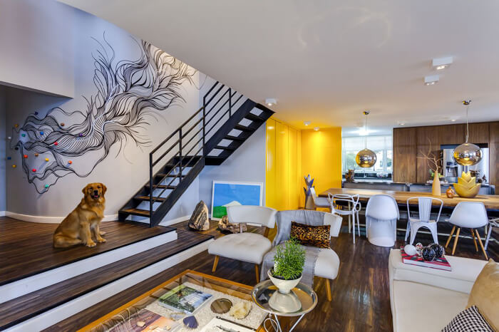 imagem de um ambiente  de sala e cozinha integrados, a parede da escada está desenhada com uma arte