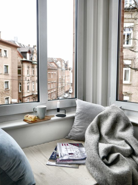 Janela de um quarto e com metade da cama e uma manta.