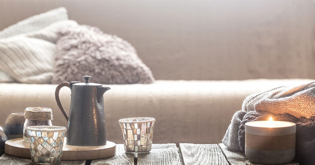 Imagem mostra uma bule com xícaras sob uma mesa de centro e um sofá ao fundo. 