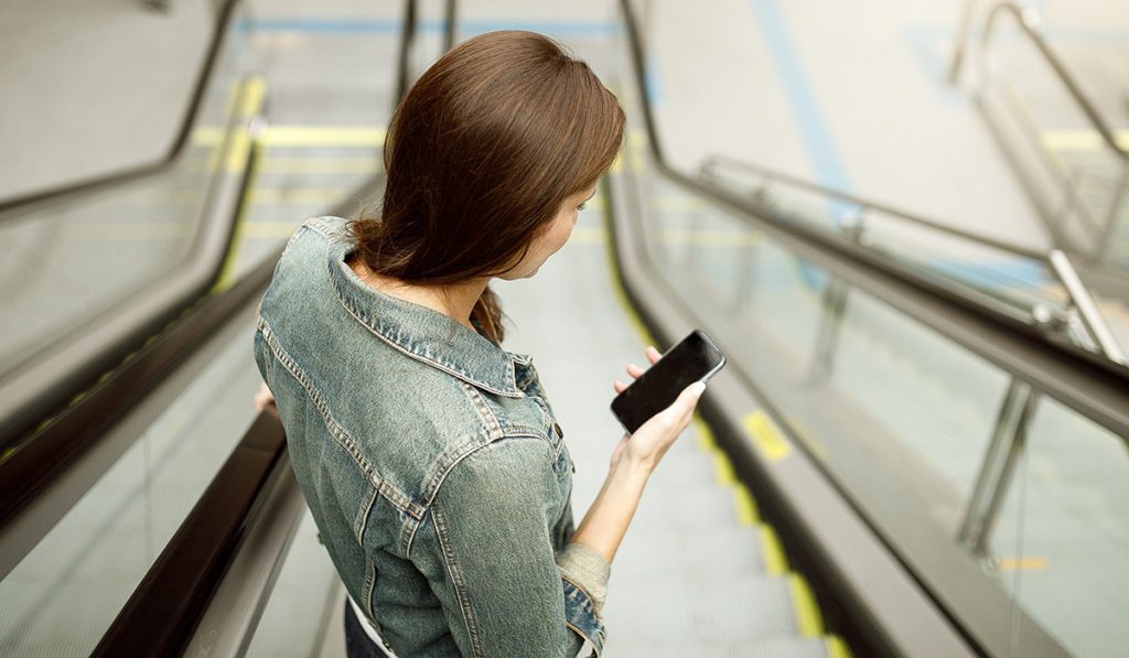 mulher com celular na mão na escada rolante